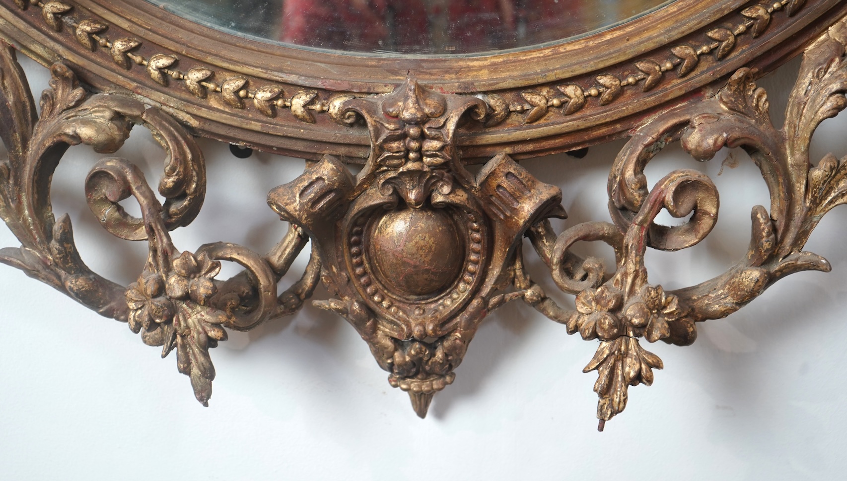 A large Louis XVI style gilt and composition girandole wall mirror, with ribbon-fold floral swag pediment over an oval plate, twin three branch sconces and open scroll cartouche apron, 105cm wide, 154cm high.